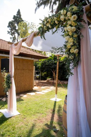 Foto de Un plano vertical de un hermoso arco de boda decorado con delicadas flores blancas en un día soleado - Imagen libre de derechos