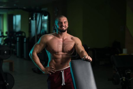 Téléchargez les photos : Un beau jeune homme caucasien et attrayant avec le corps musculaire relaxant dans la salle de gym - en image libre de droit