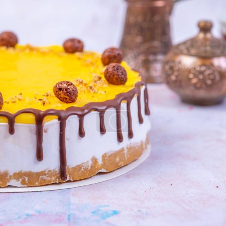 Foto de Un primer plano de la tarta de queso con una superficie amarilla decorada con crema de chocolate y bolas de chocolate sobre un fondo borroso - Imagen libre de derechos