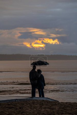 Foto de Una toma vertical de una pareja de pie y mirando hacia adelante bajo un paraguas en un día lluvioso - Imagen libre de derechos