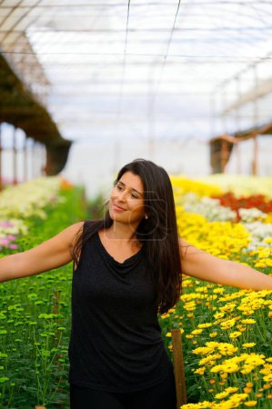 Photo for A vertical shot of a pretty Hispanic girl in a flower nursery against blurred background - Royalty Free Image