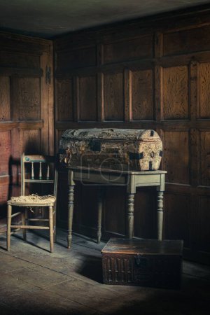 Foto de Un disparo vertical de un viejo cofre de dinero polvoriento junto a una silla en una habitación con paredes de madera - Imagen libre de derechos