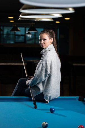 Photo for A vertical shot of a young woman sitting on the pool table. - Royalty Free Image