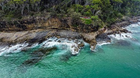 Téléchargez les photos : Une vue aérienne des vagues de l'océan turquoise frappant la côte rocheuse par une journée ensoleillée - en image libre de droit