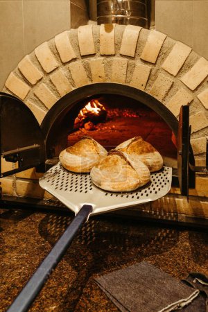 Téléchargez les photos : Un plan vertical du pain croustillant frais cuit au four étant retiré du four chaud avec la peau - en image libre de droit