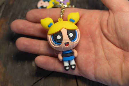Photo for Bogota, Colombia - December 22, 2022: A man showing a Bubbles keychain from the Powerpuff girls with a wooden background - Royalty Free Image