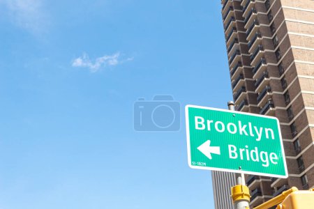 Foto de Un cartel de ubicación del puente de Brooklyn frente a un edificio y un cielo despejado en el fondo. - Imagen libre de derechos