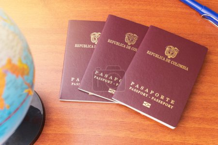 Téléchargez les photos : Trois passeports colombiens ventilés à côté d'un globe et un stylo sur un bureau en bois - en image libre de droit