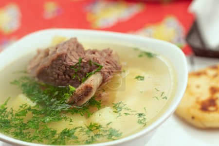 Photo for Close up of a bowl of hot soup with a piece of meat in the middle and some coriander. Rib broth with a small arepa. Concept of traditional Colombian food. - Royalty Free Image
