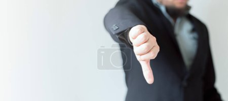 Ein Manager im Anzug zeigt vor einem unscharfen grauweißen Hintergrund missbilligend den Daumen nach unten. Konzept der schlechten Geschäftsentwicklung. Web-Banner.;