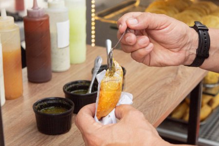 Un homme qui applique une cuillerée de sauce piquante sur une Arepa farcie aux ?ufs (Arepa de huevo con aji). Délicieux arepa frit d'origine colombienne.