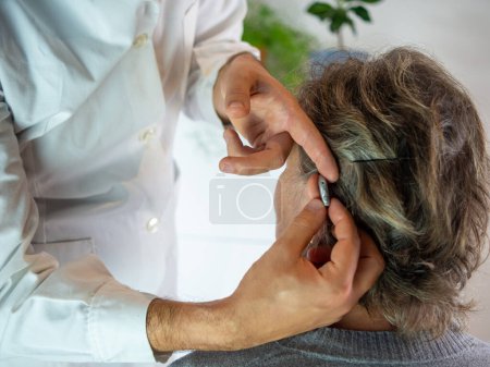 Photo for Young audiologist helping to insert an electronic hearing aid to an old woman patient - Royalty Free Image