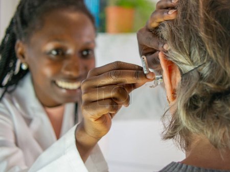 Young female audiologist helping to insert an electronic hearing aid to an old woman patient