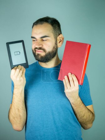 Photo for Young bearded man choosing between ebook or paper book - Royalty Free Image