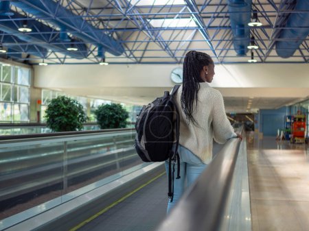 A young woman on a moving walkway inside an airport using her phone