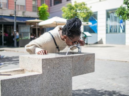 young woman drinking from a public fountain in the city