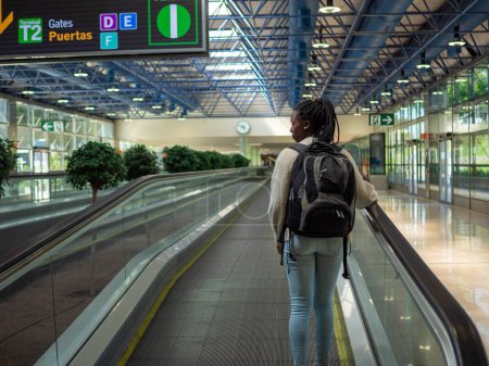 A young woman on a moving walkway inside an airport using her phone
