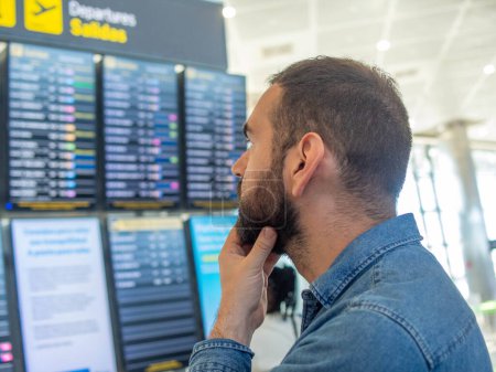 Bearded man looking at flight screens at the airport.