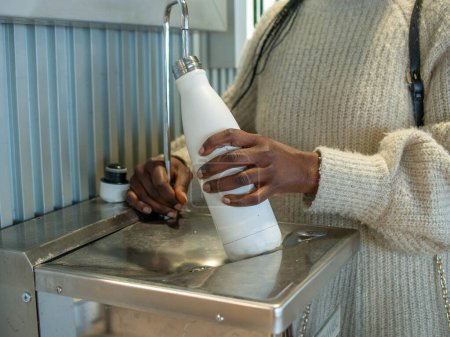 A young woman filling her reusable bottle at an airport fountain