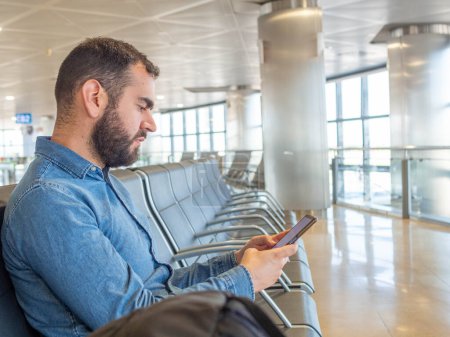 Bearded man using his smarphone while waiting in the airport terminal