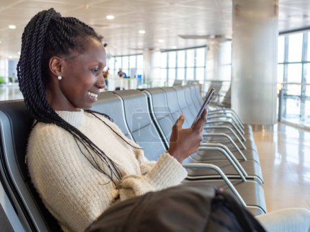 A young woman using her phone while waiting for her flight in the airport lounge