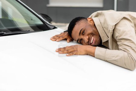 Neuer Autobesitzer. Glücklicher afroamerikanischer Mann umarmt sein nagelneues Auto Cherfully Buying Vehicle im Autohaus. Selektiver Fokus. Hochwertiges Foto