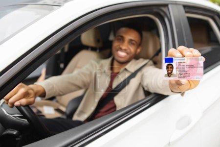 Glücklicher junger Mann aus Afrika zeigt seinen Führerschein aus dem offenen Autofenster. Hochwertiges Foto