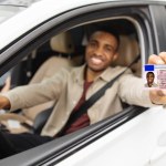 Happy young african man showing his drivers license from open car window. High quality photo