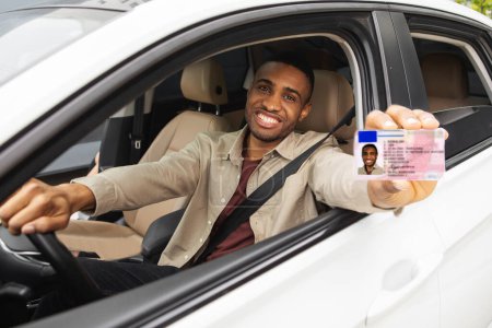 Glücklicher junger Mann aus Afrika zeigt seinen Führerschein aus dem offenen Autofenster. Hochwertiges Foto