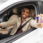 Happy young african man showing his drivers license from open car window. High quality photo