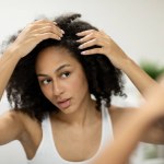 Portrait of a beautiful young woman examining her scalp and hair in front of the mirror, hair roots, color, grey hair, hair loss or dry scalp problem. High quality photo