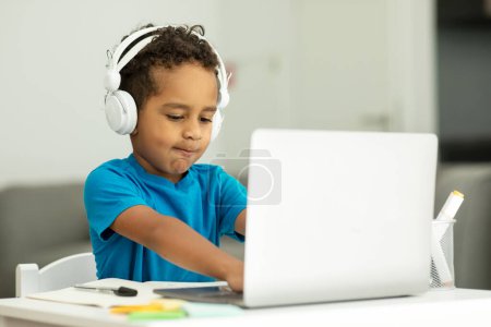 Photo for Portrait of a student in a headset, sitting on a chair at a table, using a computer, talking to a teacher or friends. High quality photo - Royalty Free Image