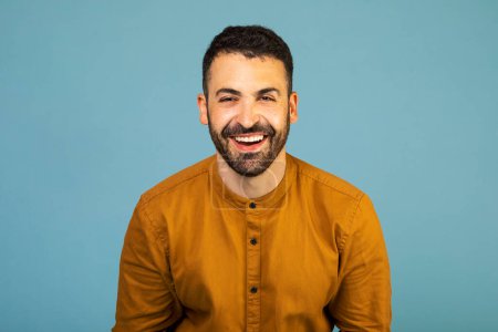 Foto de Cheerful man smiling happily at camera, posing isolated over blue studio background, free space. People, youth, emotions concept - Imagen libre de derechos