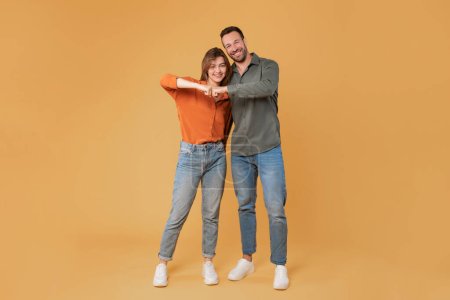 Photo for Smiling happy couple man and woman giving a fist bump in agreement, looking and smiling at camera, posing together on orange background. Full length shot - Royalty Free Image
