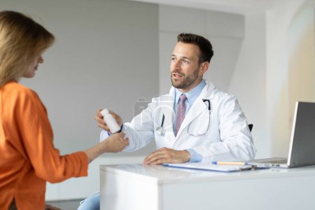 Téléchargez les photos : Médecin homme prescrivant des médicaments à la patiente après le check-up à la clinique, thérapeute homme donnant des vitamines à la jeune femme - en image libre de droit
