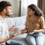 Angry indian couple having quarrel experiencing crisis in relationship, sitting on sofa and having conflict at home. Marital problems, divorce concept