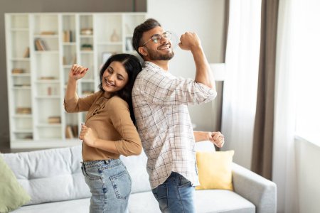 Young indian spouses dancing at home in living room, couple having fun, enjoying spending time together on weekend at home