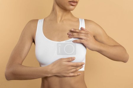 Téléchargez les photos : Concept d'auto-dépistage mammaire. Jeune femme en soutien-gorge blanc faire un bilan pour la prévention du cancer, fond studio beige, gros plan - en image libre de droit