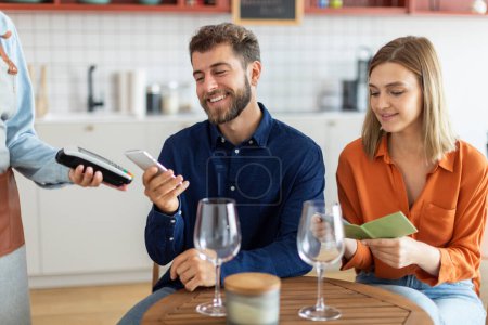 Photo for Couple in cafe, man client pay bill order use cellphone near field communication system. Modern fast easy tech NFC contactless payment - Royalty Free Image