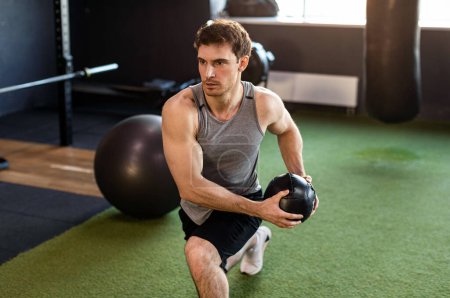 Jeune homme fort faisant de l'exercice avec la médecine balle dans la salle de gym, ayant séance d'entraînement le matin