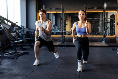 Persönliches Training für zwei. Fitness Mann und Frau machen Ausfallübungen zum Aufwärmen und Verbrennen der Beinmuskulatur, modernes Fitnessstudio-Interieur
