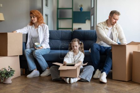 Photo for Upset daughter helping mom and dad packing belongings in cardboard boxes, relocating sitting on sofa in living room together - Royalty Free Image