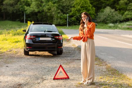 Lady standing near sign of broken car in the middle of the highway and trying to call for help. Car service concept