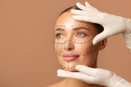 Photo for Portrait of young woman and plastic surgeon making marks on female face over beige studio background, preparing for facelifting procedure - Royalty Free Image