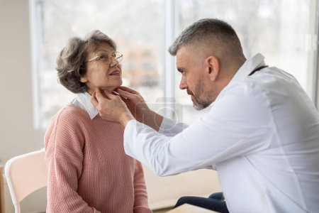 Professioneller Arzt tastet Hals einer älteren Patientin ab, während er sie während der Konsultation in der Privatpraxis untersucht