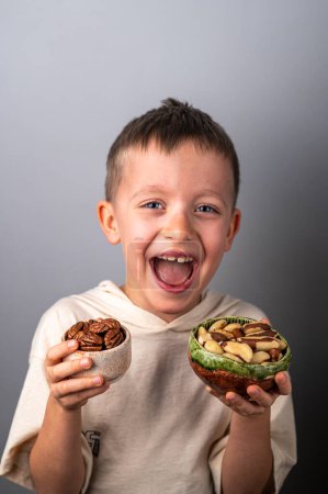 Foto de Niño alegre elige entre diferentes nueces. Pecana pelada y nuez de Brasil. Alimentación saludable. - Imagen libre de derechos