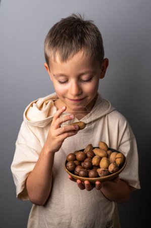 Foto de Niño sosteniendo un tazón con nueces de pacana y macadamia. Comida y merienda saludables. - Imagen libre de derechos