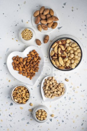 Photo for Different types of nuts on a plate in the shape of a heart. Assorted nuts on a white background. Top view. - Royalty Free Image