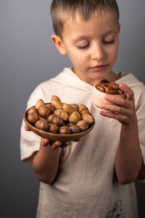 Photo for A little boy chooses between different nuts. Macadamia nuts and pecans. Healthy Eating. - Royalty Free Image