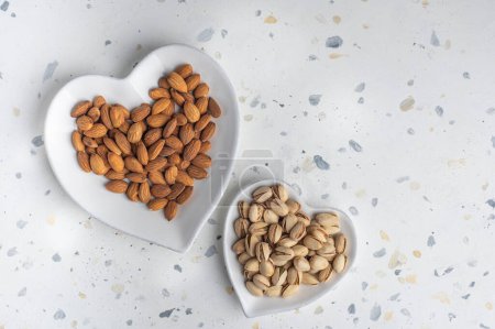 Photo for Almonds and pistachios in heart-shaped plates. Top view. Place for text - Royalty Free Image